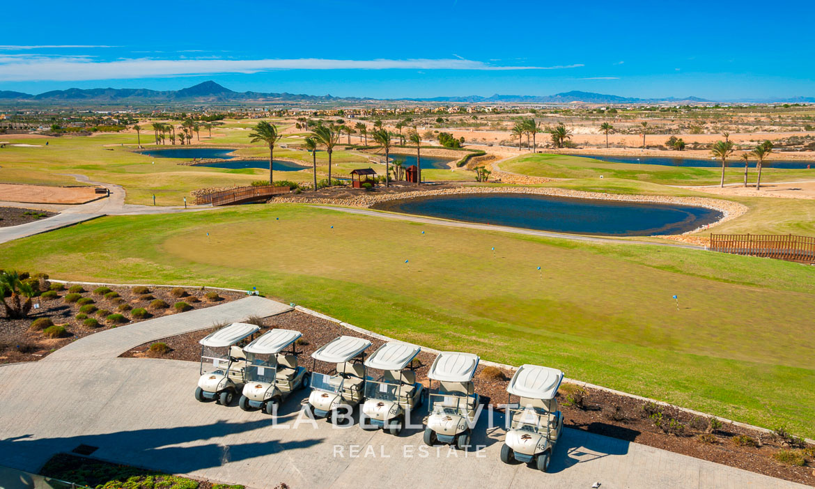 Panoramic sun-drenched golf course with golf carts and scenic mountains near Hacienda del Álamo single-storey villa, Murcia.