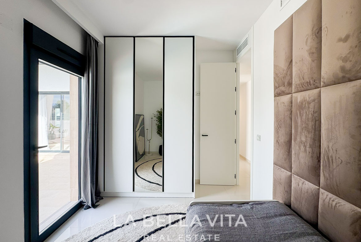 Bright, modern bedroom with reflective wardrobe, plush headboard, and sunlit terrace in a new 3-bedroom villa in San Miguel de Salinas.