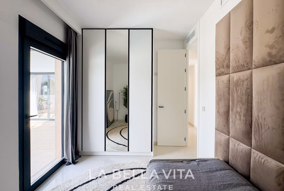Bright, modern bedroom with reflective wardrobe, plush headboard, and sunlit terrace in a new 3-bedroom villa in San Miguel de Salinas.