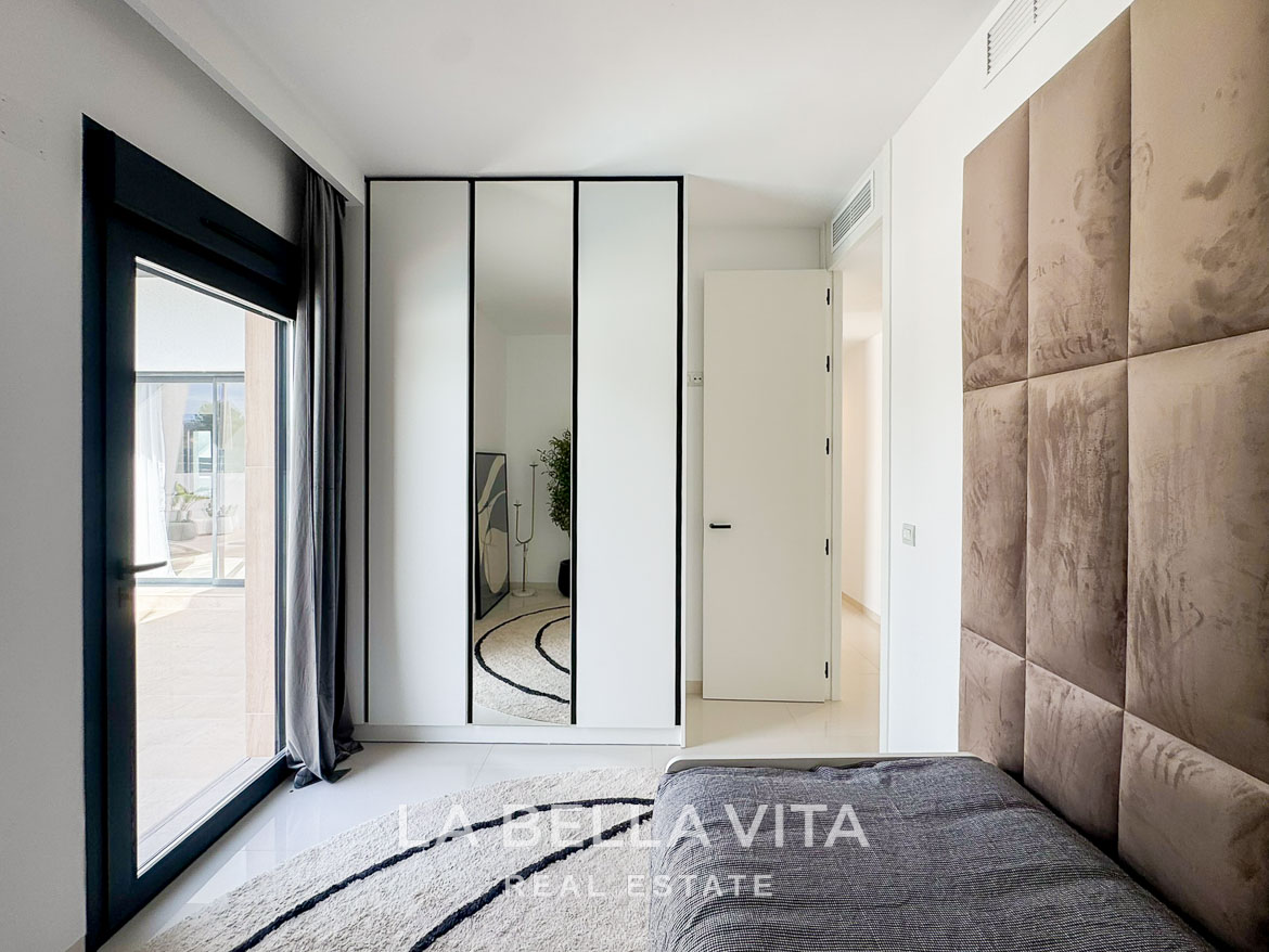 Bright, modern bedroom with reflective wardrobe, plush headboard, and sunlit terrace in a new 3-bedroom villa in San Miguel de Salinas.