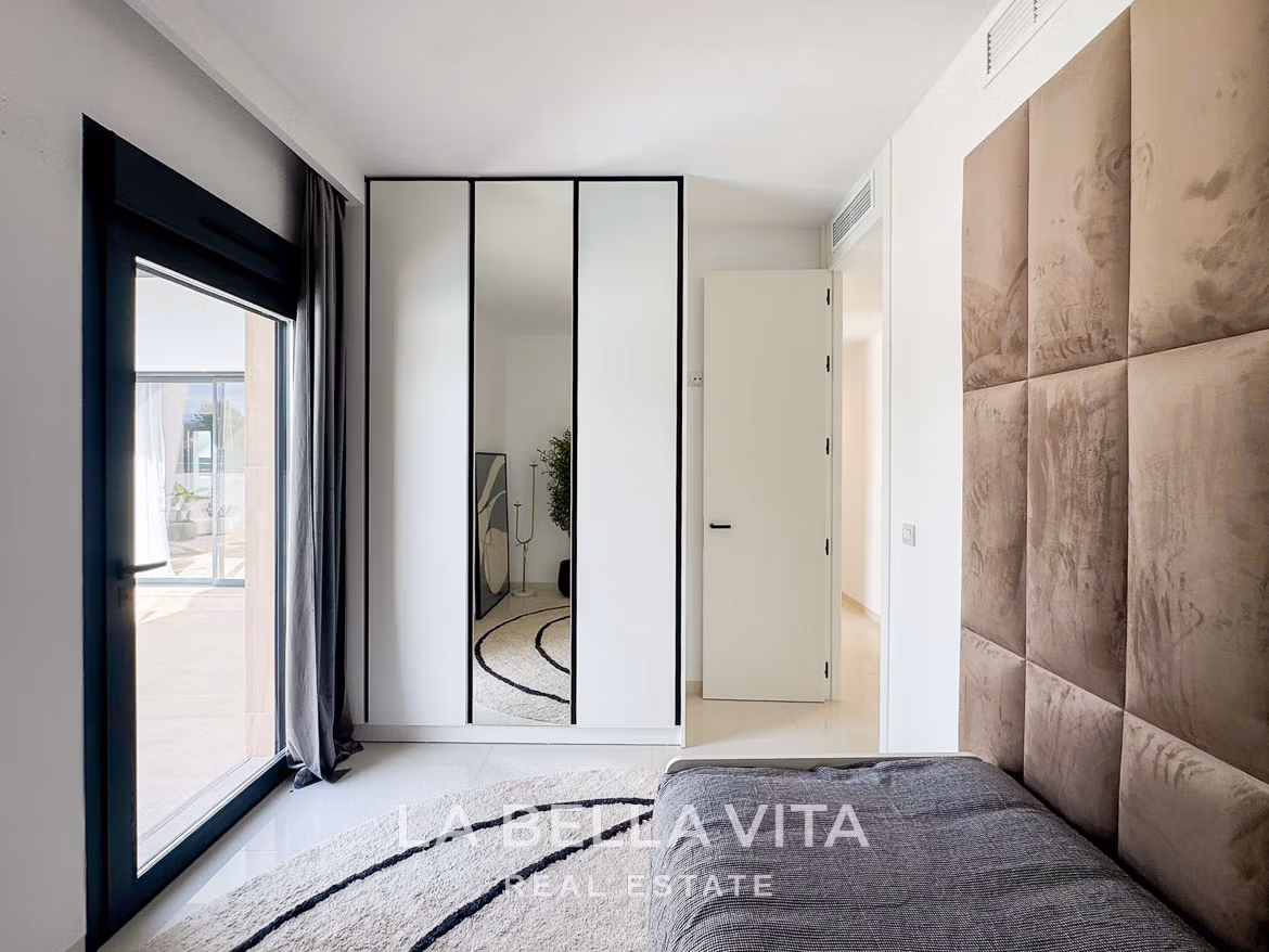 Bright, modern bedroom with reflective wardrobe, plush headboard, and sunlit terrace in a new 3-bedroom villa in San Miguel de Salinas.