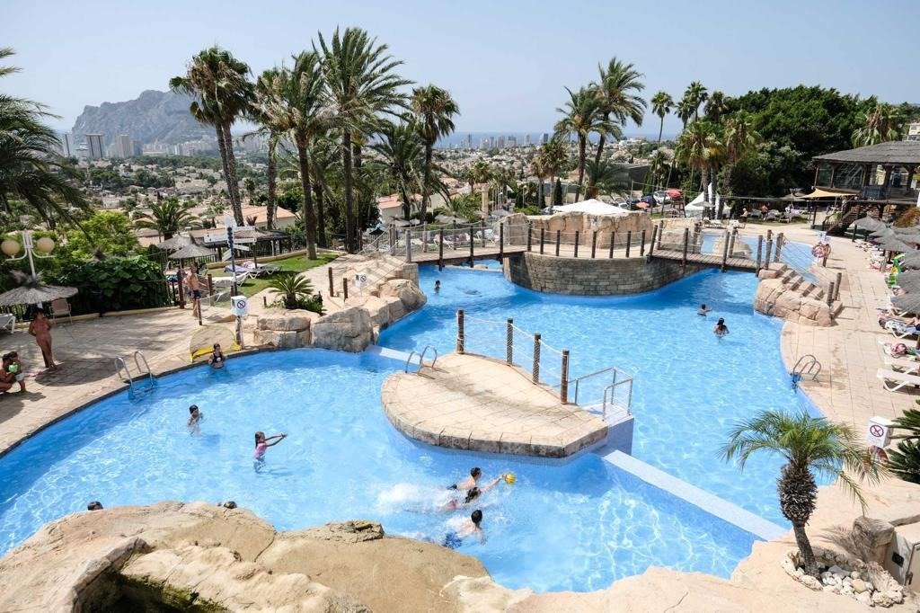 Sun-drenched, spacious pool area with tropical landscaping at top floor bungalow apartments in Calpe, overlooking the sea and mountains.