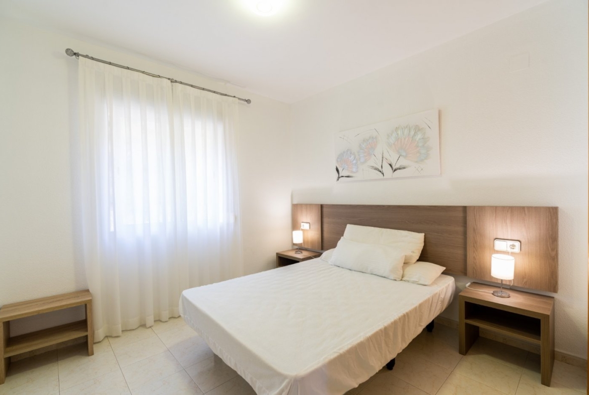 Bright and minimalist bedroom in top floor bungalow apartment in Calpe with soft natural light and modern wooden furnishings.