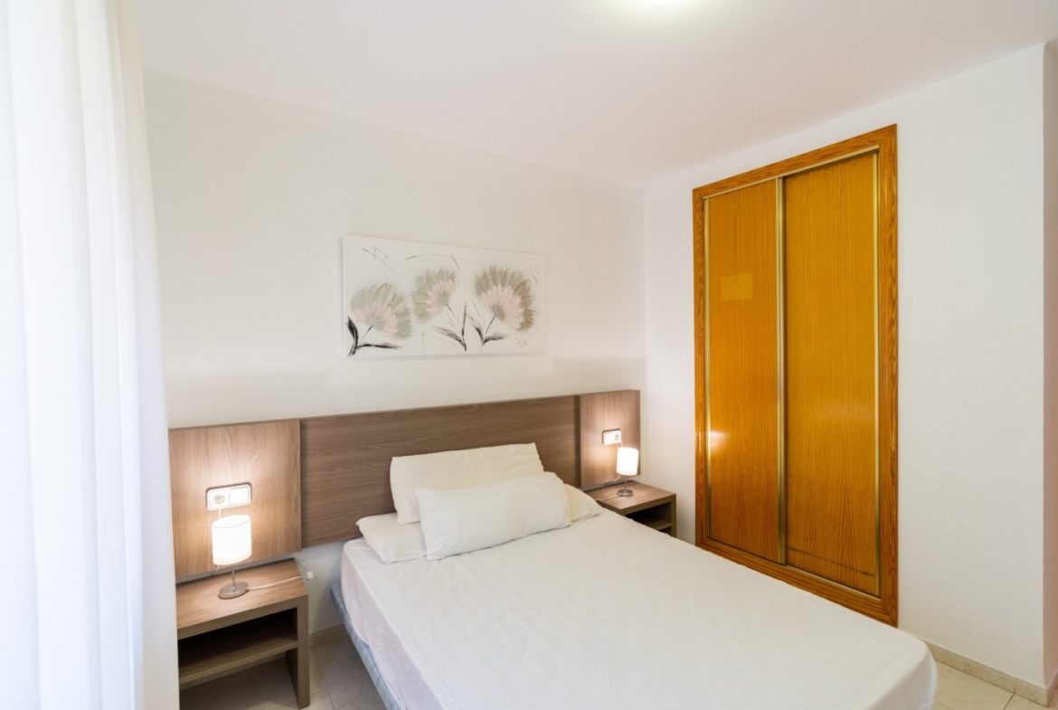 Bright, cozy bedroom with elegant wood accents in a top floor bungalow apartment in Calpe, featuring modern lighting and soft décor.