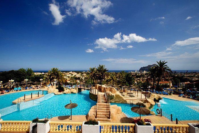 Panoramic sun-drenched pool area with lush palm trees at top floor bungalow apartments in Calpe, overlooking the sea and town.