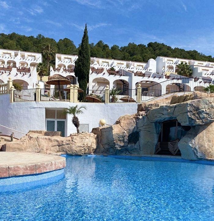 Sun-drenched top floor bungalow apartments in Calpe with whitewashed exteriors, private terraces, and a sparkling blue pool with rock features.