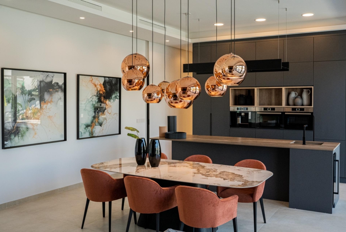 Modern bespoke villa dining area in Ciudad Quesada with elegant marble table, plush terracotta chairs, and copper pendant...