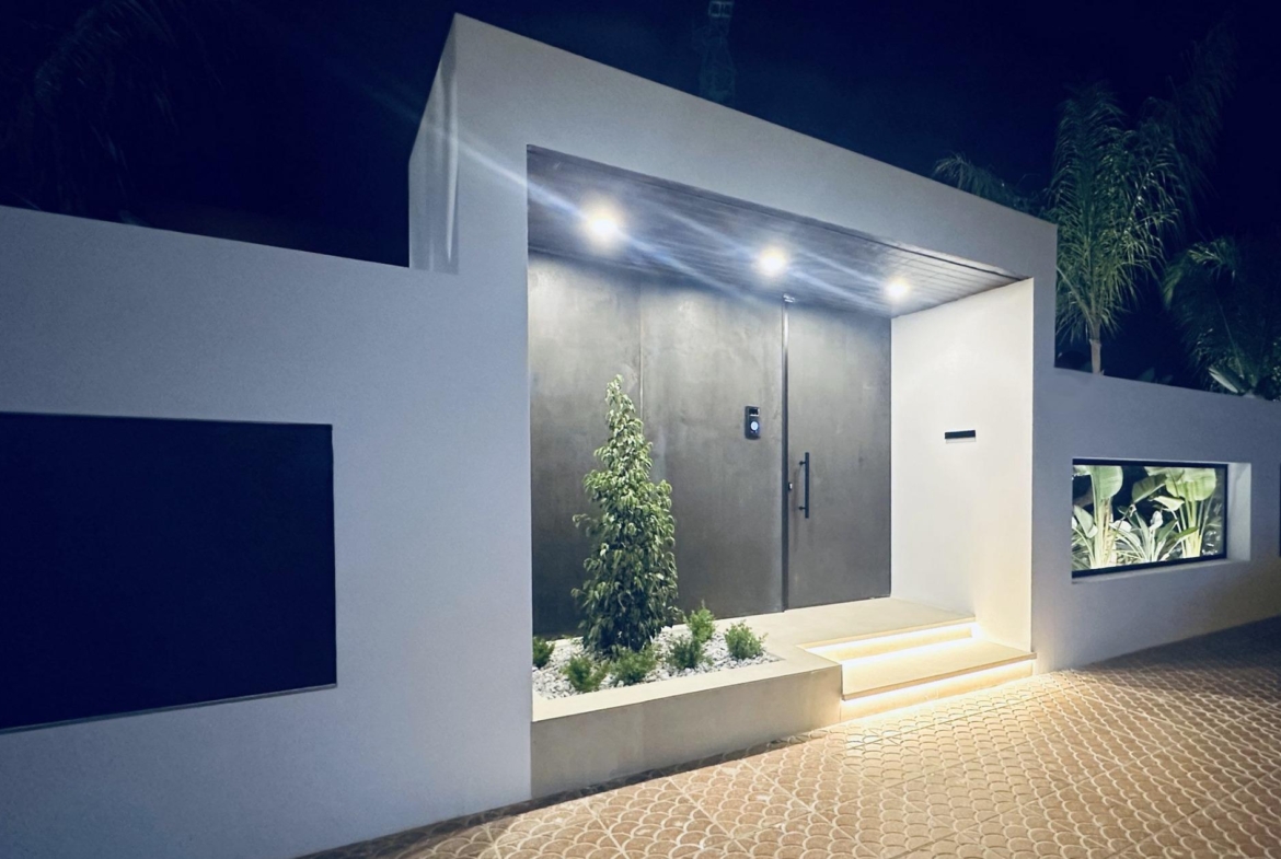 Sleek modern villa entrance in Ciudad Quesada with illuminated black door, white walls, minimalist landscaping, and palm...