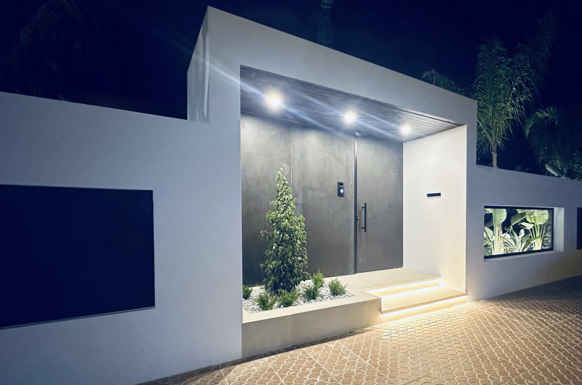 Sleek modern villa entrance in Ciudad Quesada with illuminated black door, white walls, minimalist landscaping, and palm...