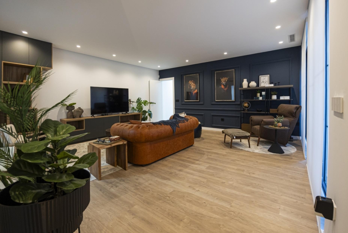 Spacious modern living room in bespoke 3-bedroom villa with leather sofa, dark accent wall, and natural wood flooring in...