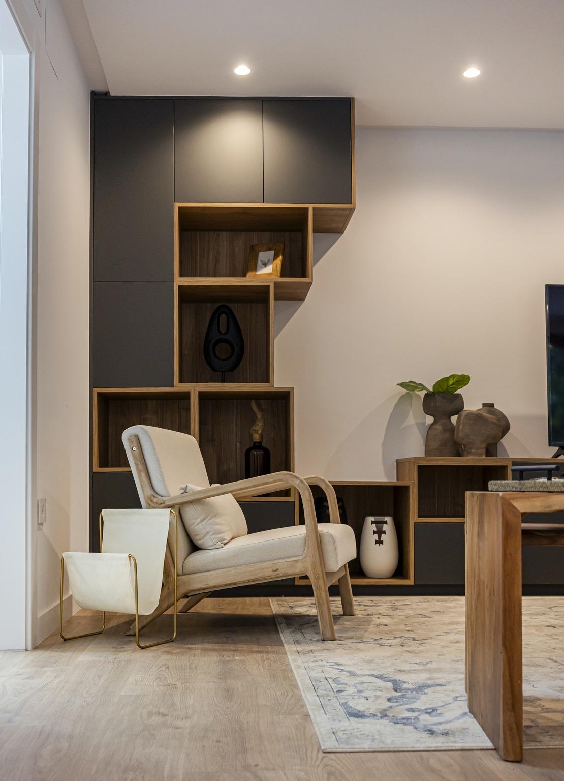 Bright and elegant living room corner in bespoke villa, featuring sleek wooden shelving, cream armchair, and decorative...