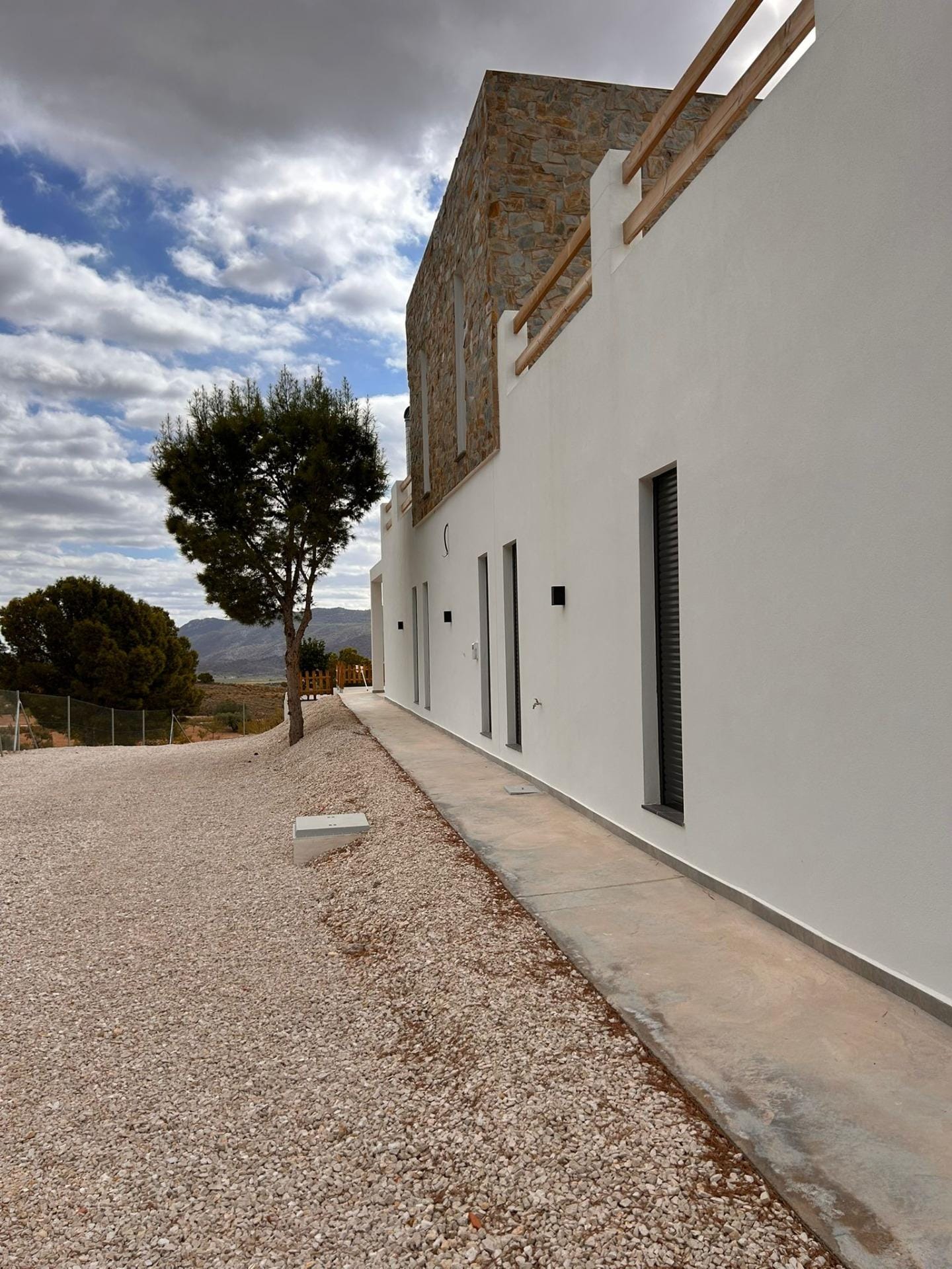 Custom-Built-New-Villas-in-Pinoso-Alicante-Spacious-Homes-in-Natural-Surroundings-26 Side path along a white villa facade and gravel garden in Pinoso, Alicante
