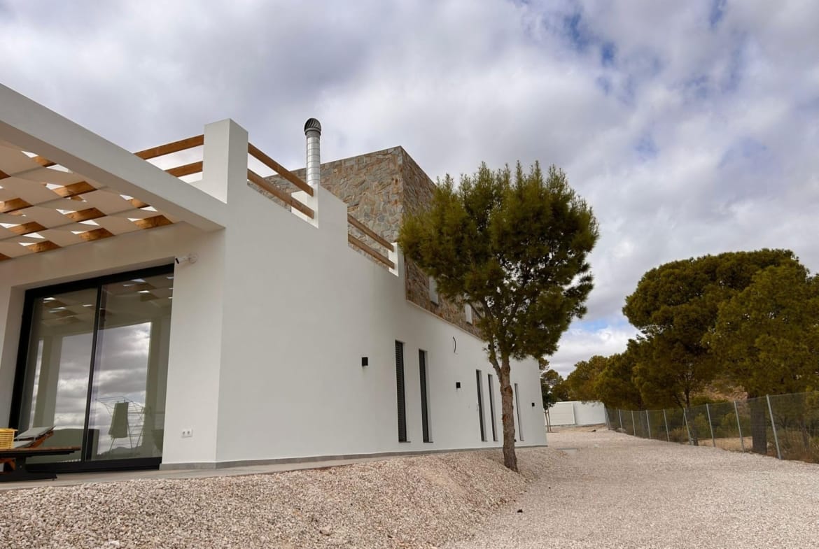 Villa exterior and gravel garden beside mature trees in Pinoso, Alicante