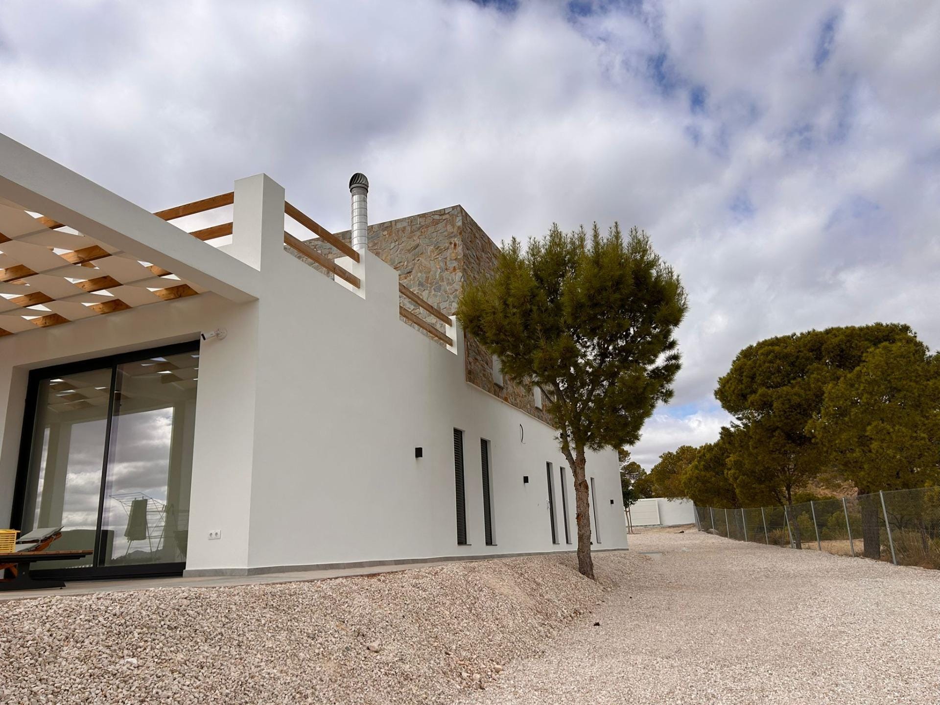 Custom-Built-New-Villas-in-Pinoso-Alicante-Spacious-Homes-in-Natural-Surroundings-27 Villa exterior and gravel garden beside mature trees in Pinoso, Alicante