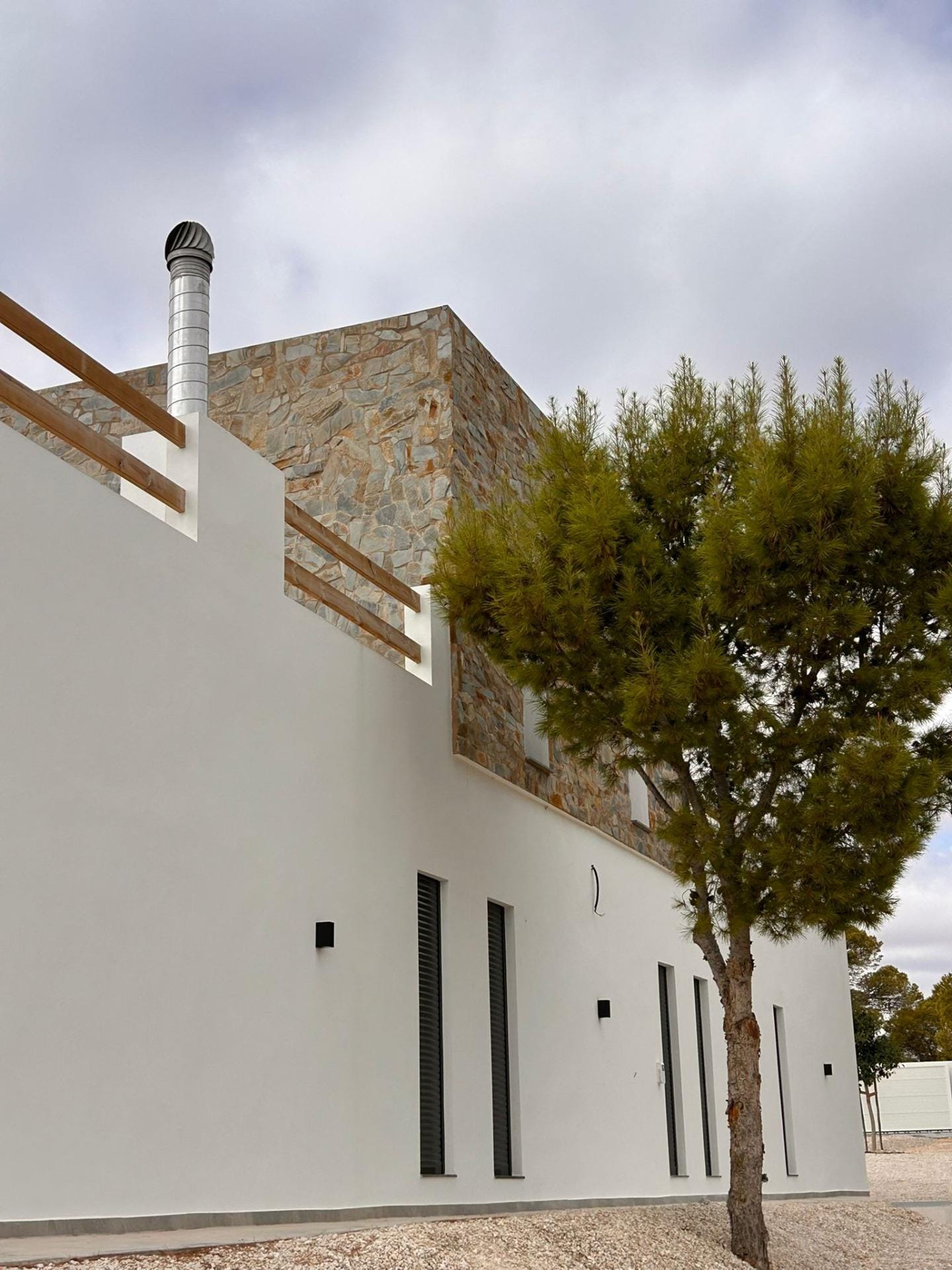 Custom-Built-New-Villas-in-Pinoso-Alicante-Spacious-Homes-in-Natural-Surroundings-28 Villa side facade with an upper terrace and stone cladding in Pinoso, Alicante