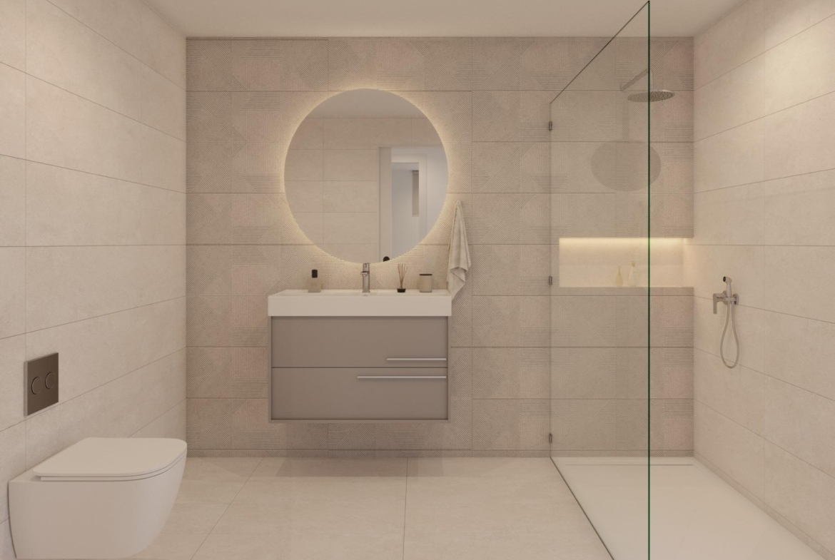 Bathroom with wall-mounted toilet, vanity unit and round backlit mirror beside glass shower