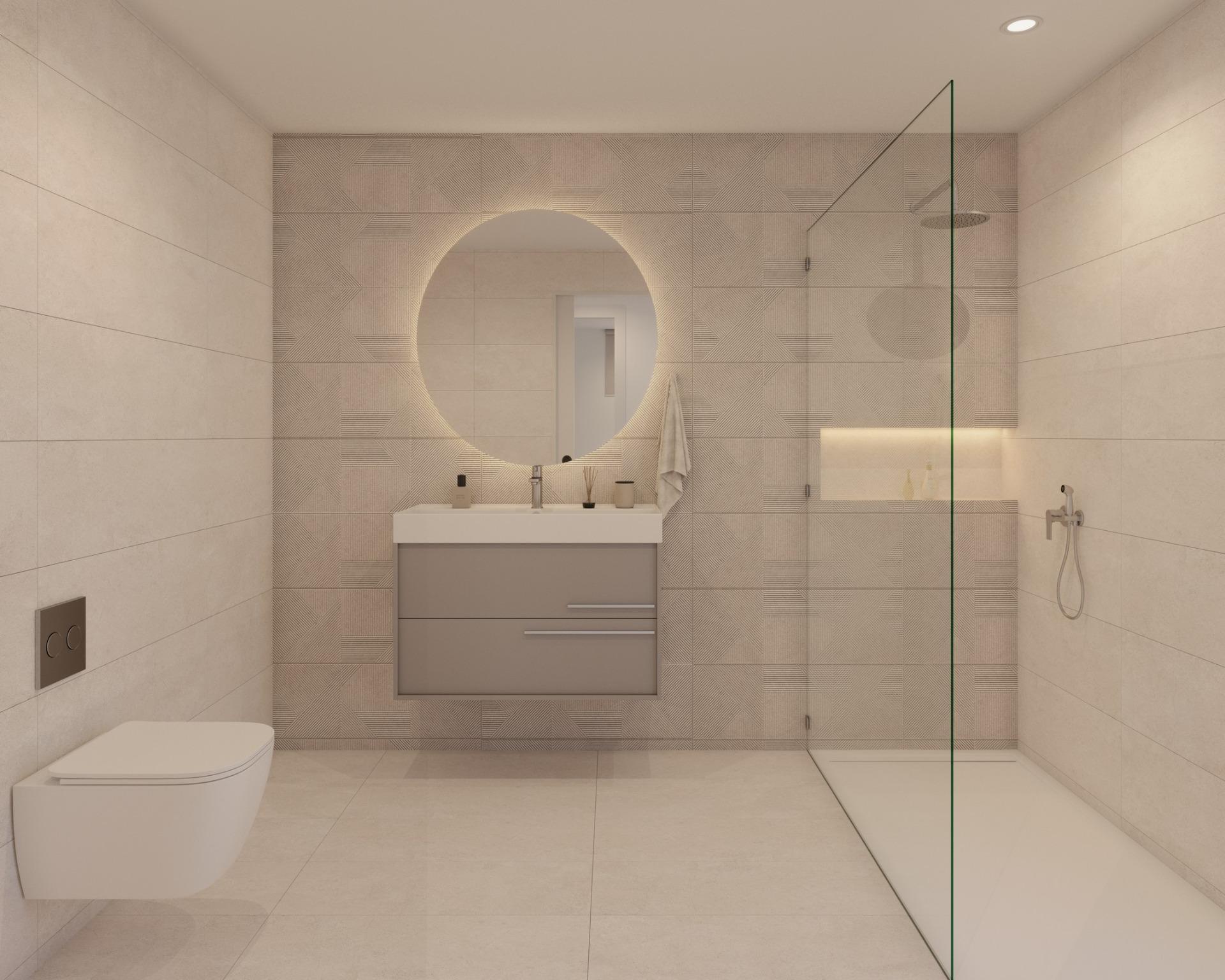 Bathroom with wall-mounted toilet, vanity unit and round backlit mirror beside glass shower
