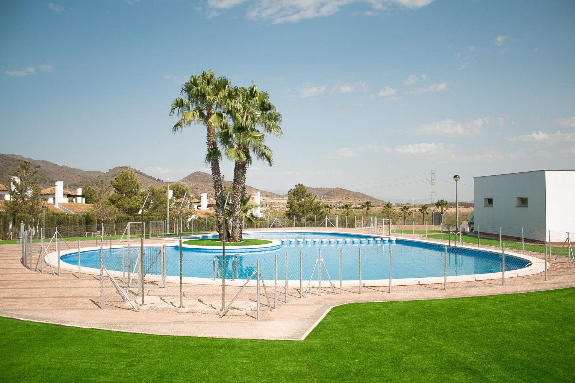 KEY-READY-VILLA-IN-FUENTE-ALAMO-MURCIA-40 Curved communal swimming pool beside lawns and mountain scenery in Las Palas, Fuente Álamo, Murcia