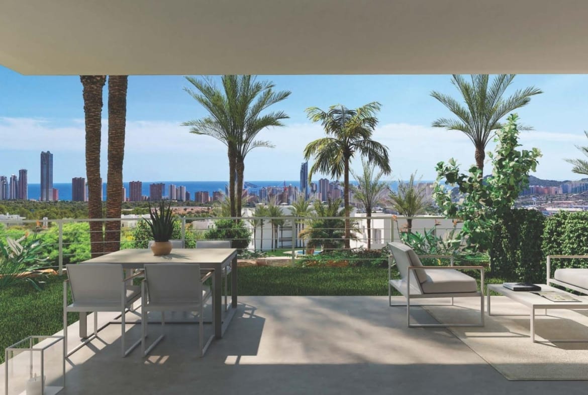 Covered terrace with a dining table, lounge chairs, palm trees and a distant coastal skyline in Sierra Cortina, Alicante