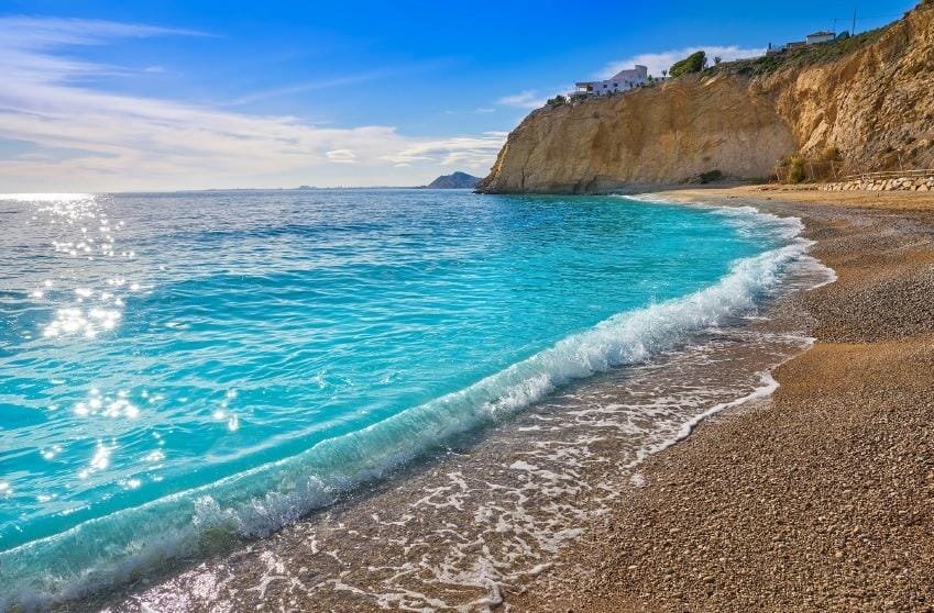Turquoise water beside a pebble beach and rocky cliffs on the Villajoyosa coast, Alicante