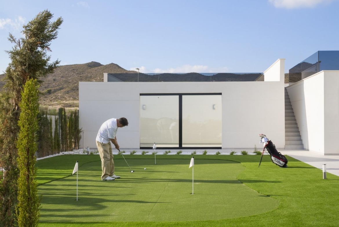 Man practising on a small private putting green with the villa facade behind him