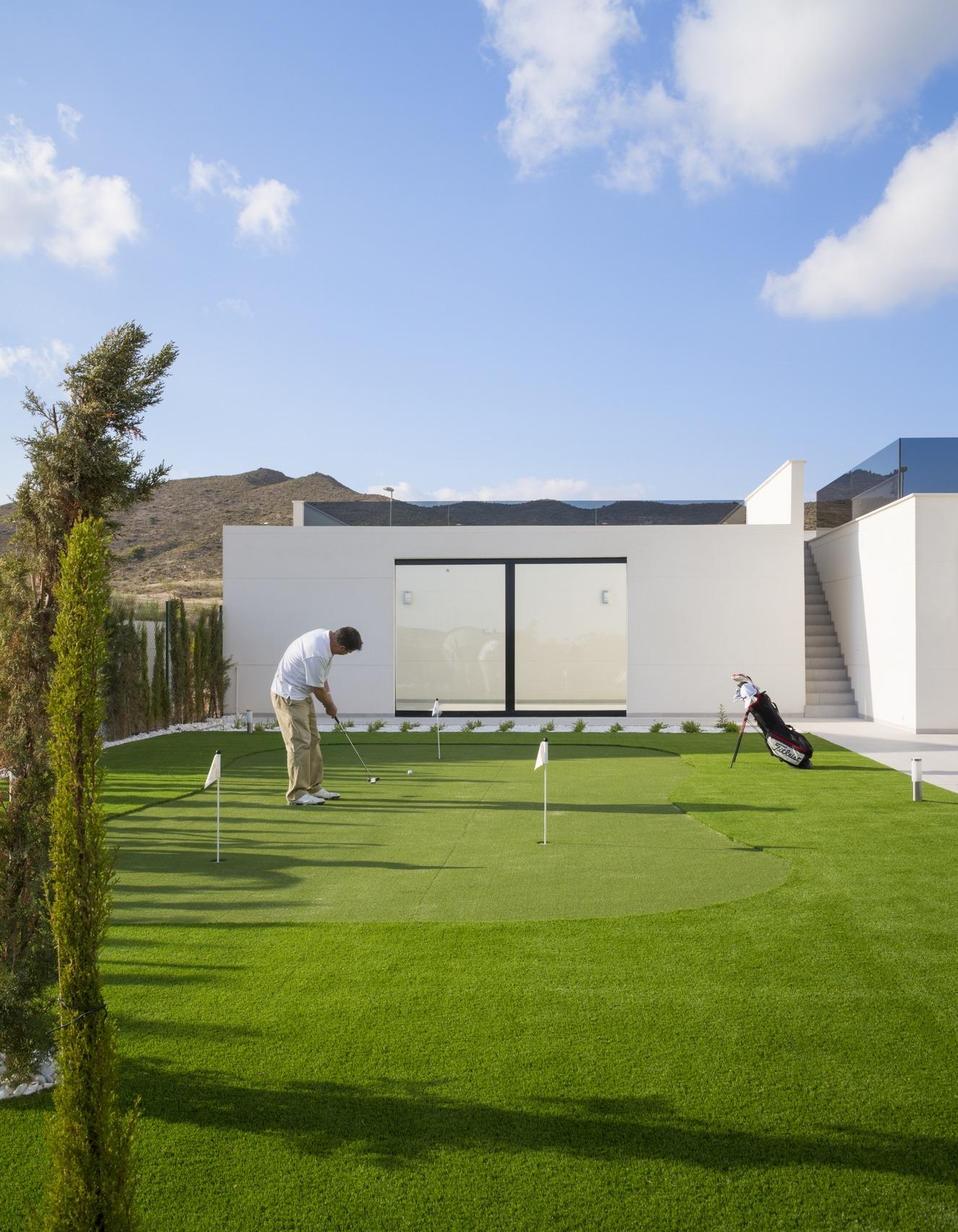 Man practising on a small private putting green with the villa facade behind him
