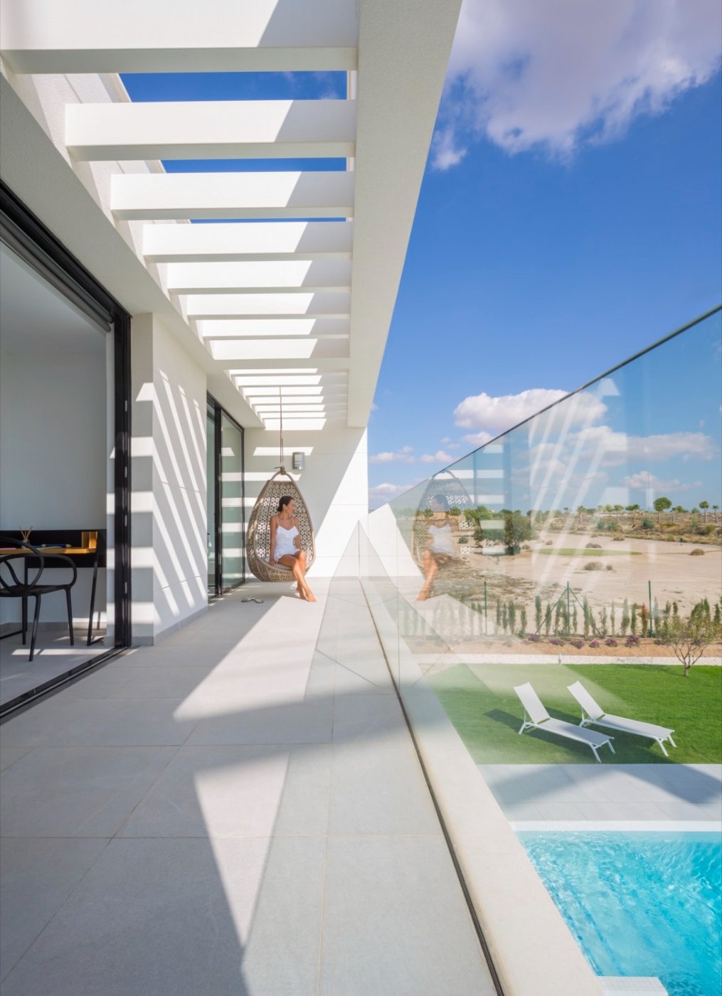 Long balcony with hanging chair, glass balustrade and pool visible below