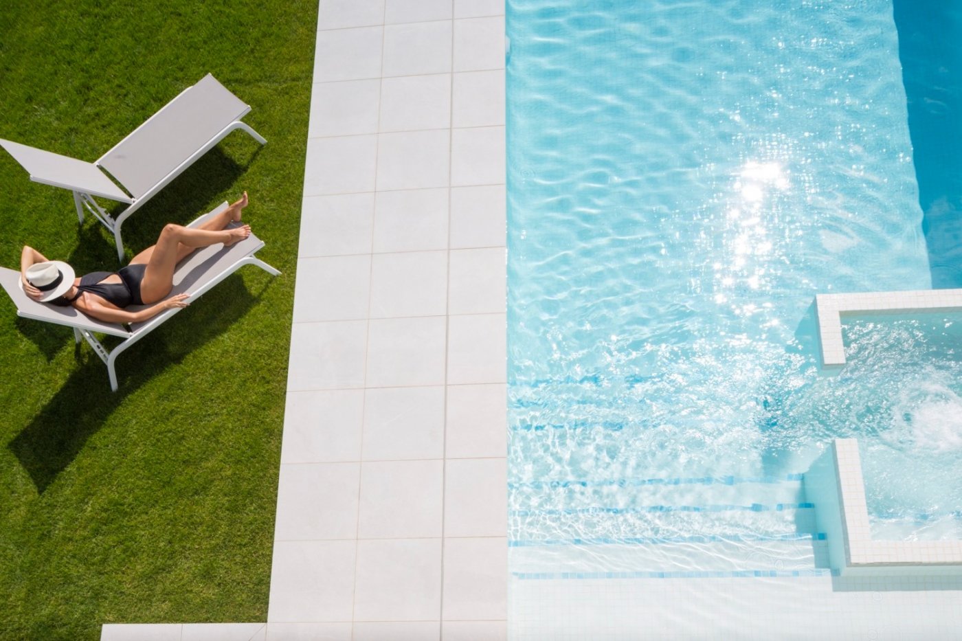 Woman reclining on a sunlounger beside a tiled terrace and bright blue pool