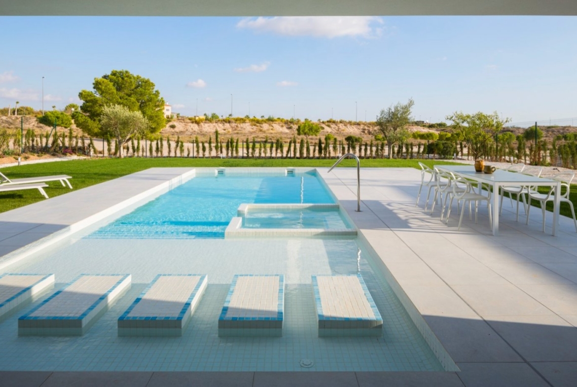 Rectangular pool with submerged loungers, adjacent dining table and lawn beyond