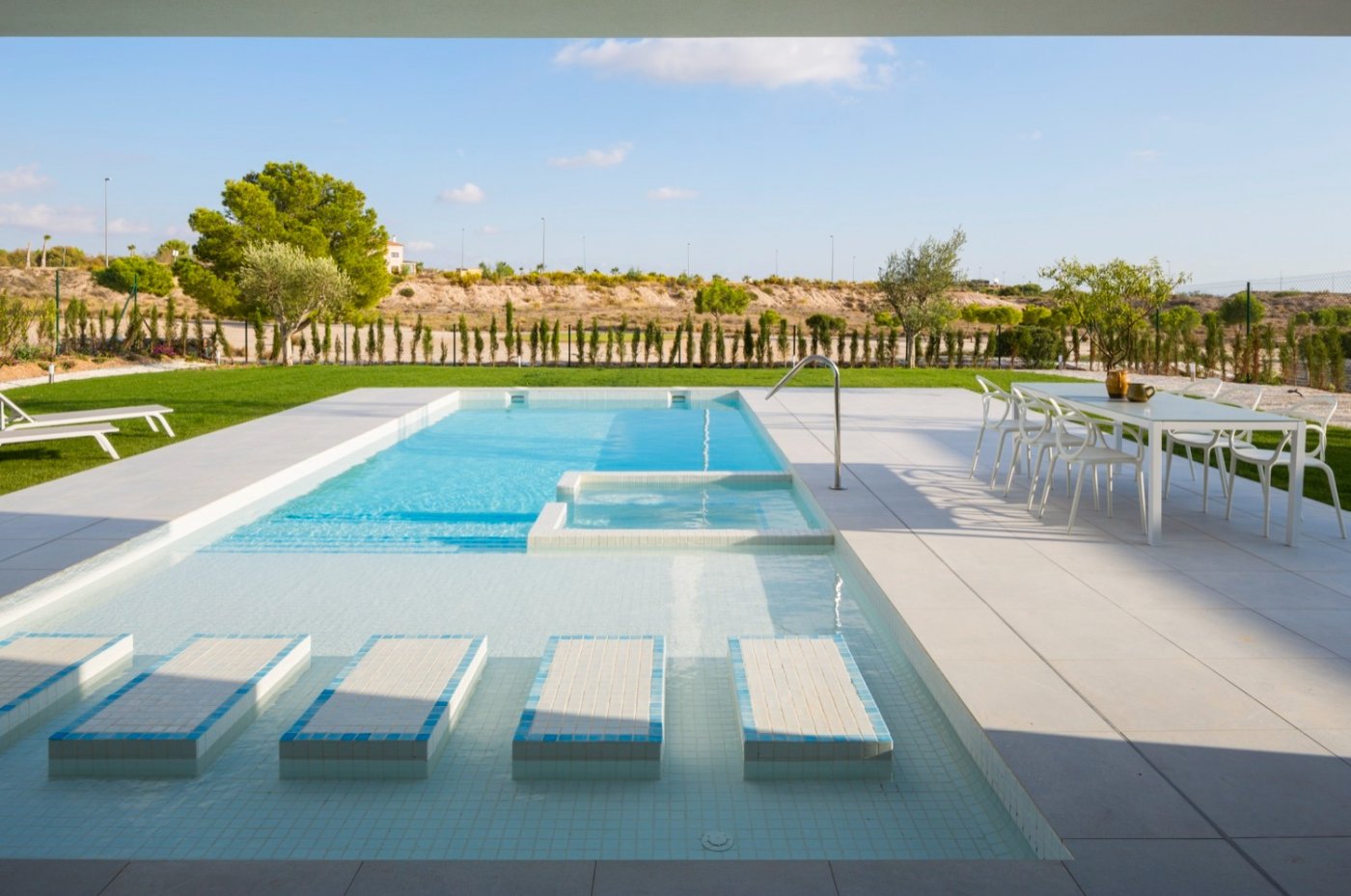 Rectangular pool with submerged loungers, adjacent dining table and lawn beyond