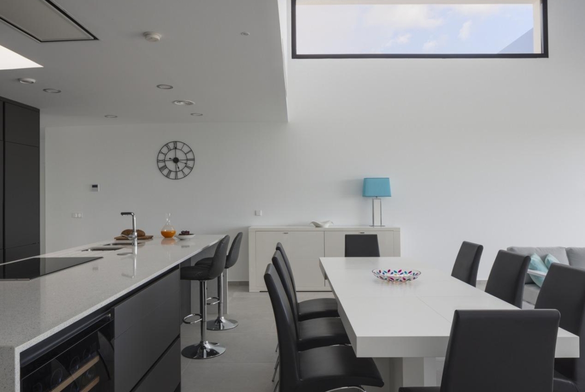 White dining table beside long dark kitchen island and visible built-in wine fridge