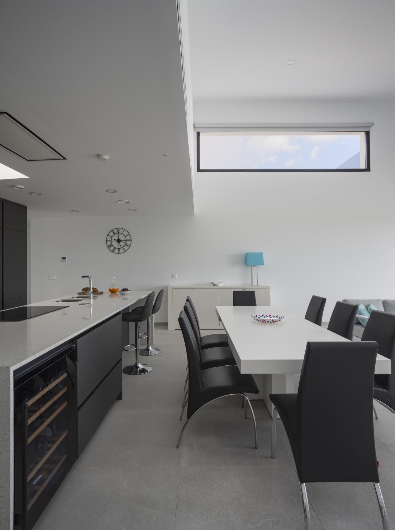 White dining table beside long dark kitchen island and visible built-in wine fridge