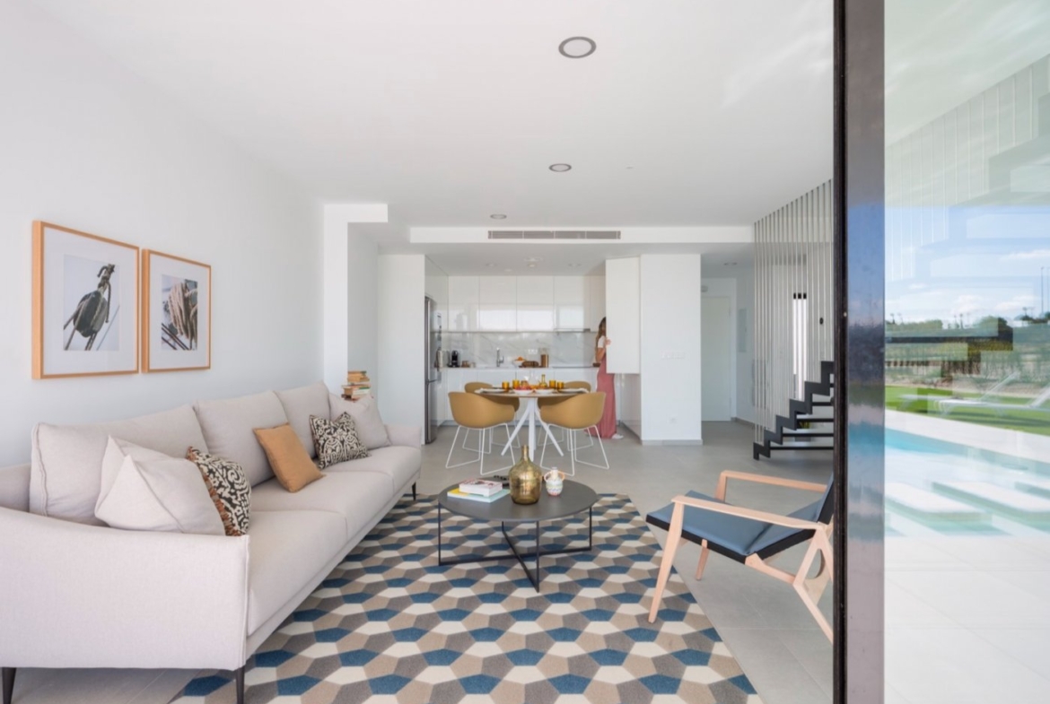 Living room looking toward white kitchen and dining area, geometric rug on floor