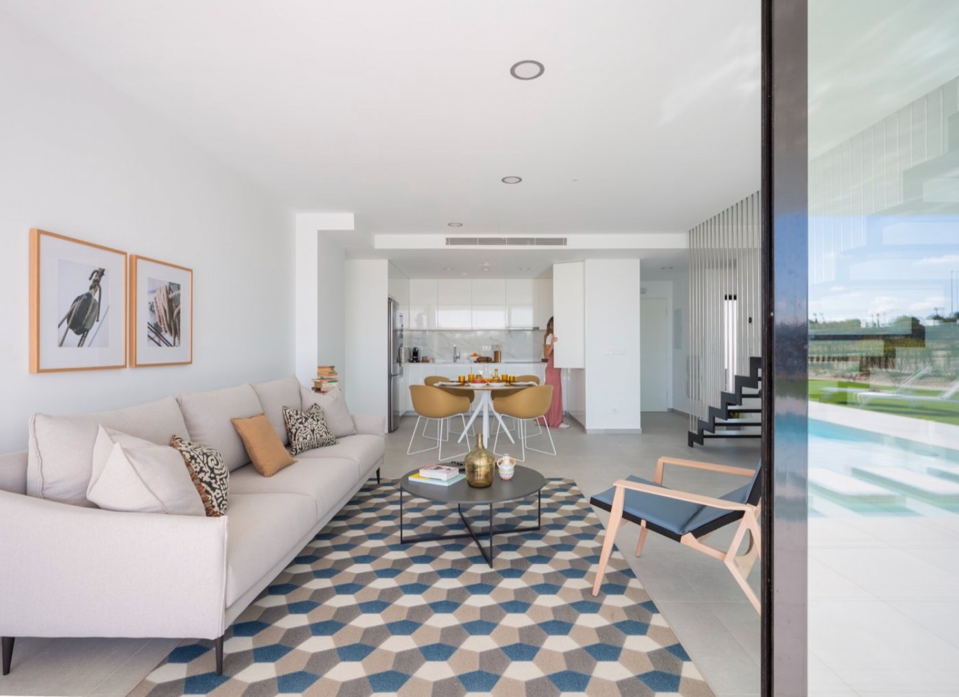 Living room looking toward white kitchen and dining area, geometric rug on floor