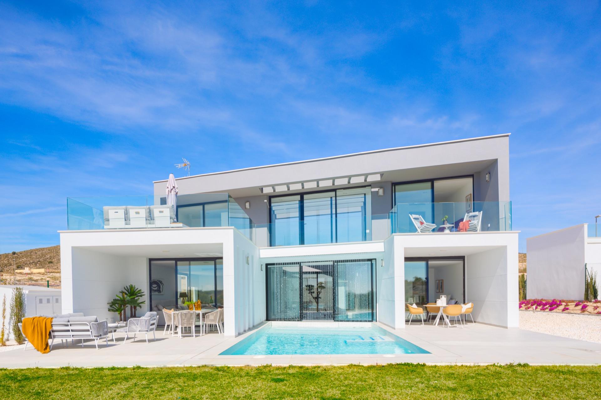 Front view of a two-storey white villa with pool, terrace seating and glass balustrade