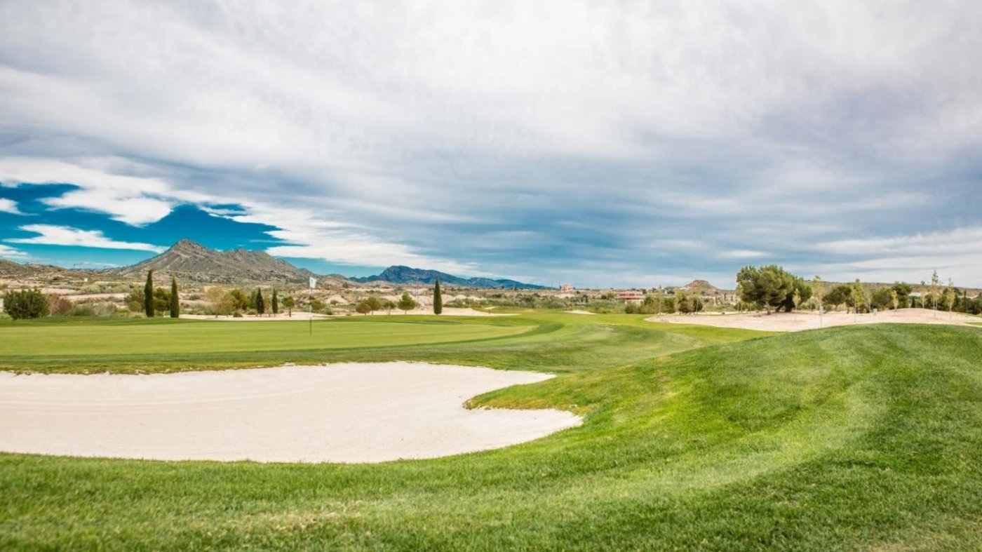 Wide view across a golf fairway showing sand bunker and rolling green landscape