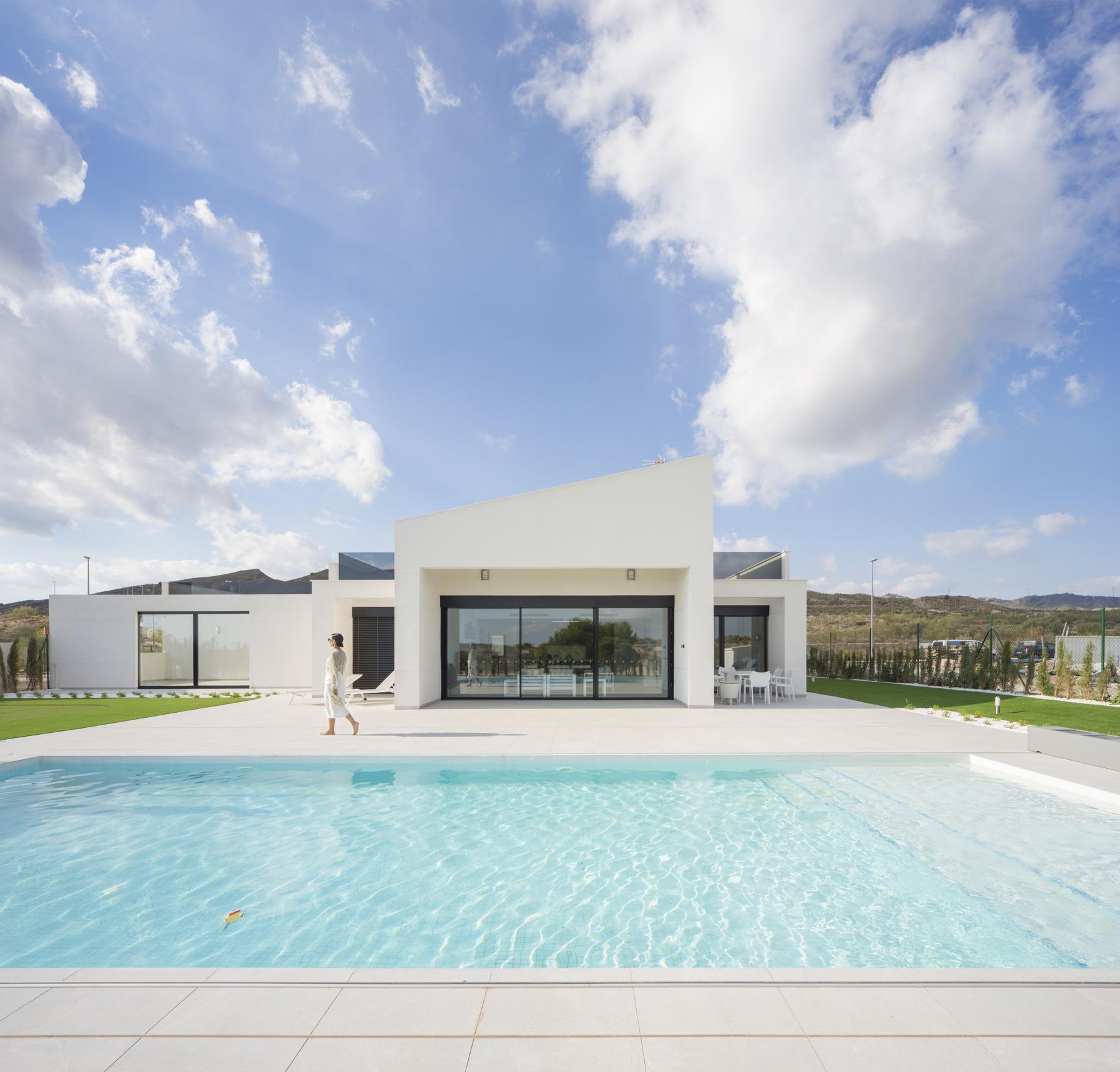 Single-storey white villa rear facade with pool, terrace and a person walking nearby