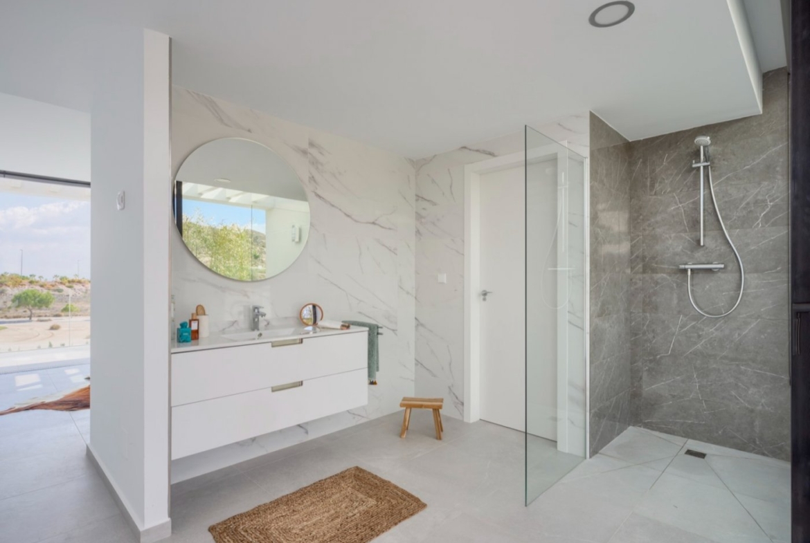 Bathroom with circular mirror, white vanity unit and walk-in shower area