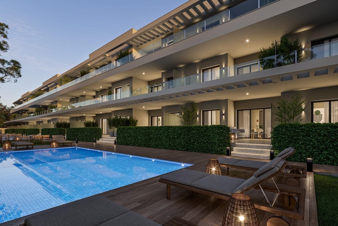 Apartment balconies beside a lit communal swimming pool and sun loungers at dusk in Los Narejos, Murcia