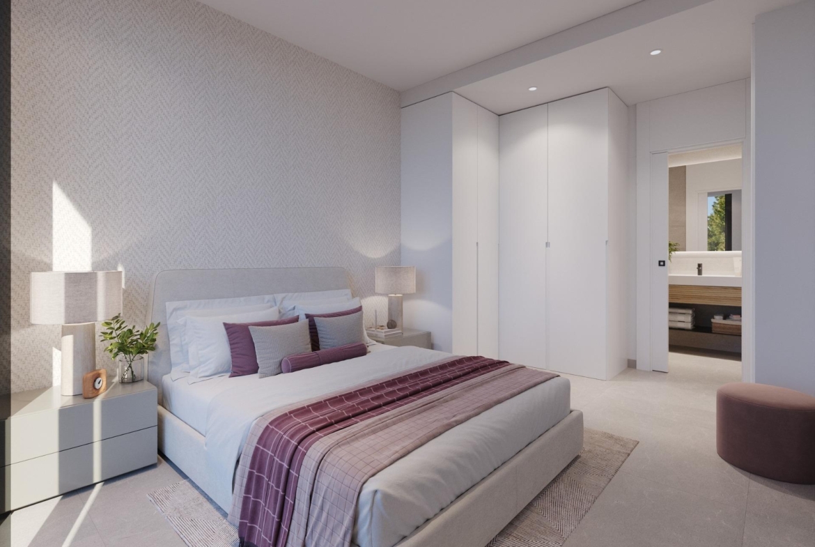Bedroom with bedside table, lamps and white built-in wardrobes leading to bathroom