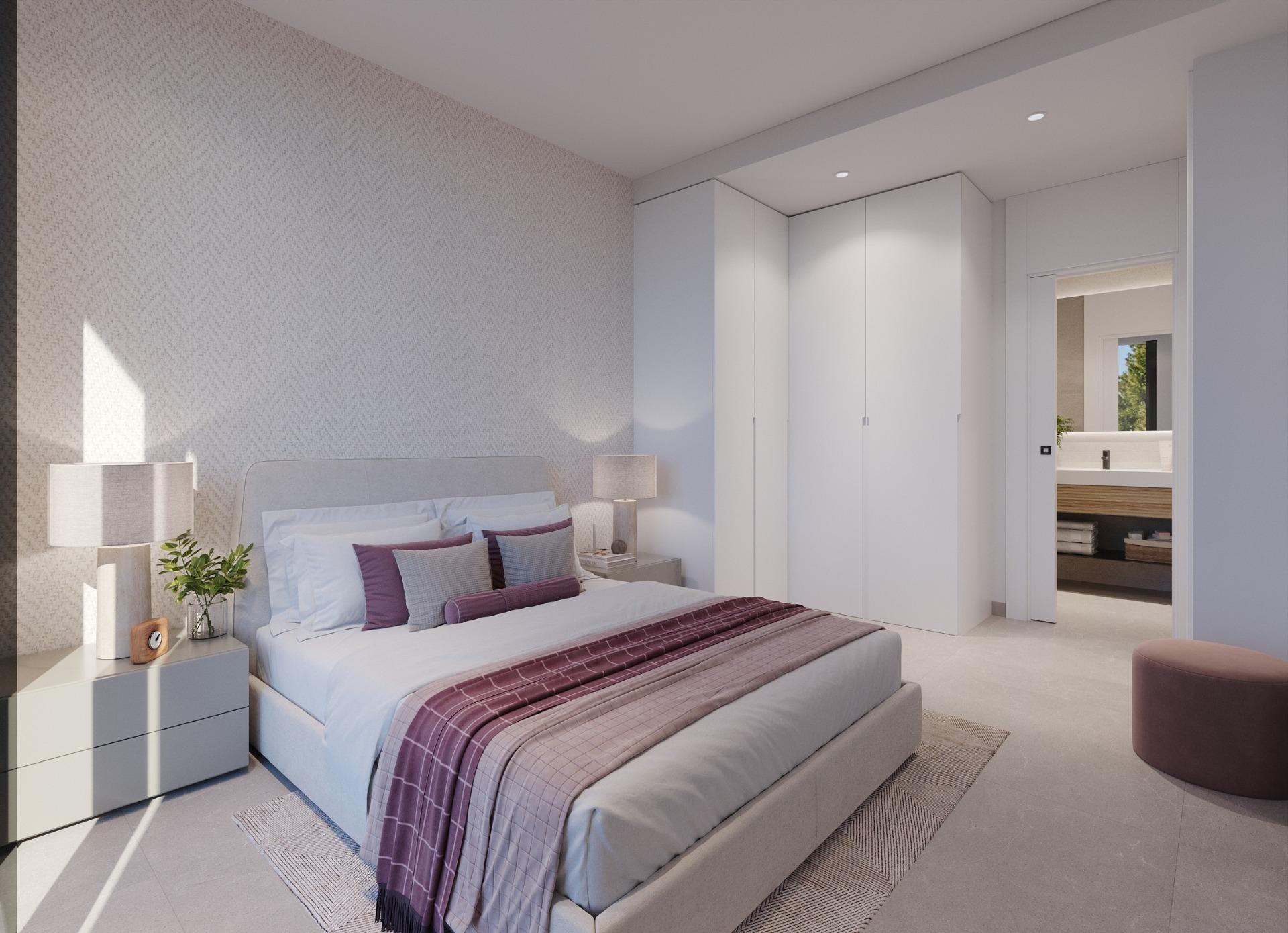 Bright bedroom with padded headboard, bedside lamp and built-in white wardrobes by doorway