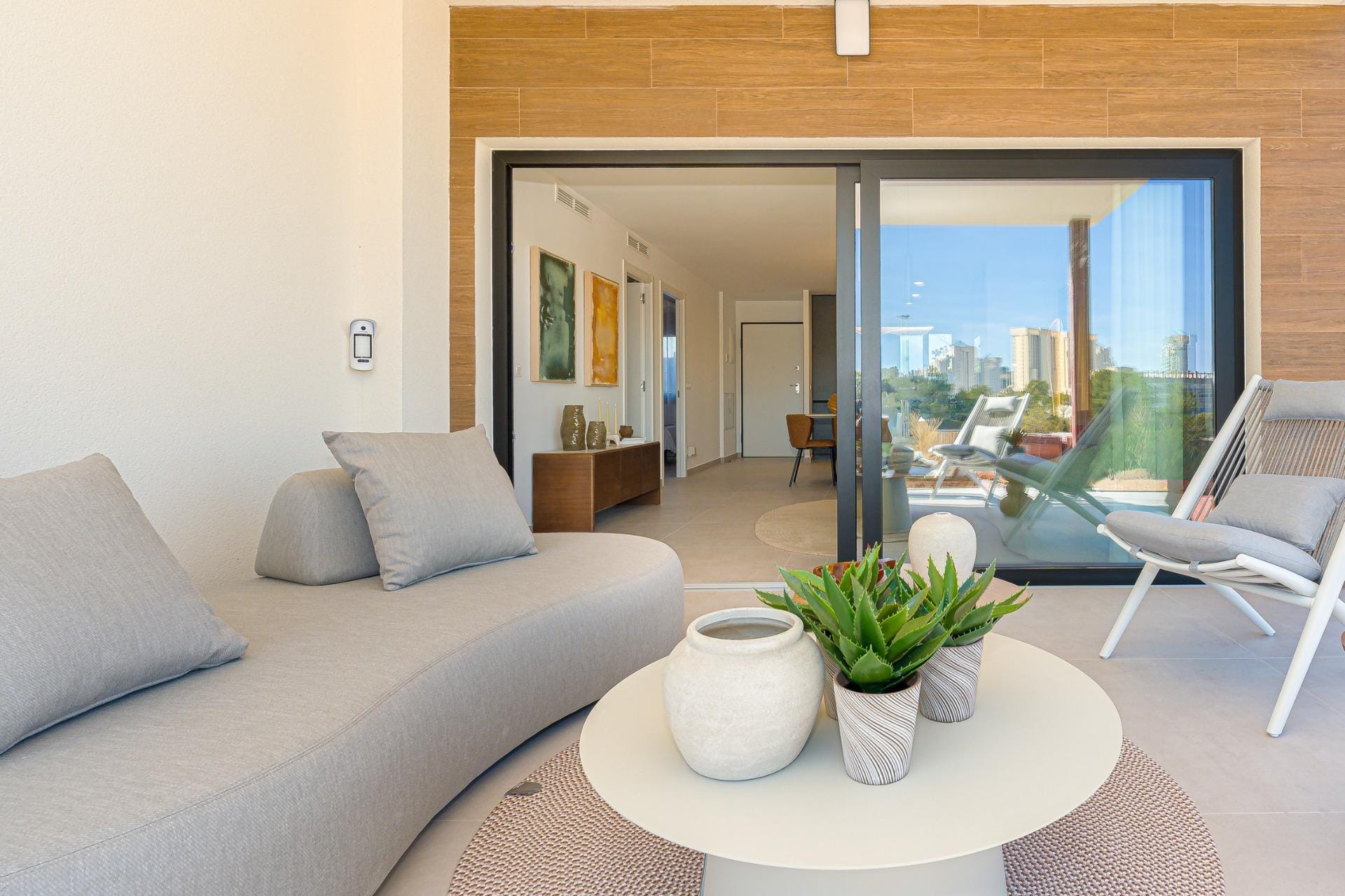 Covered terrace with lounge seating opening into a bright modern apartment