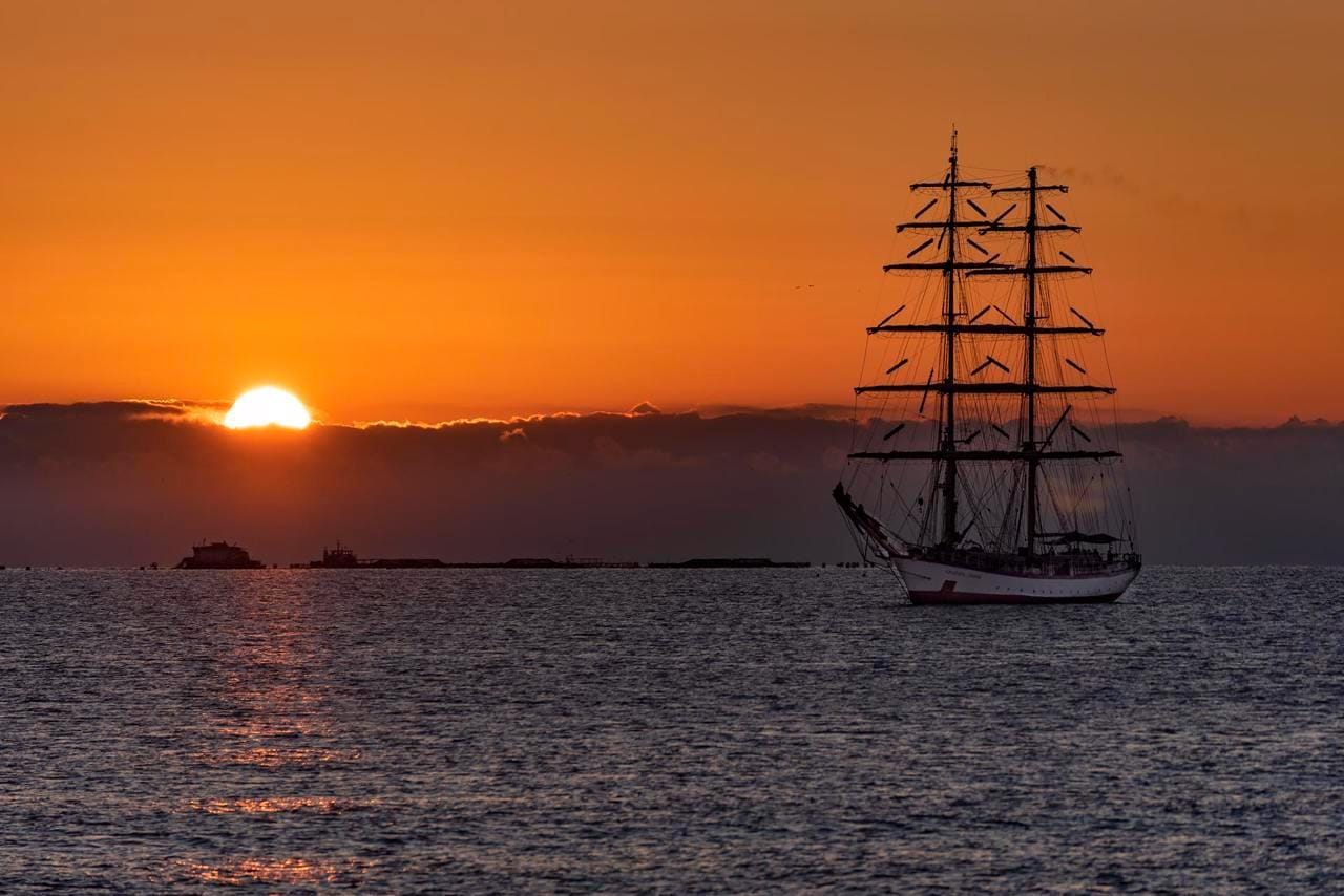 Sailing ship silhouetted against an orange sunset over the sea