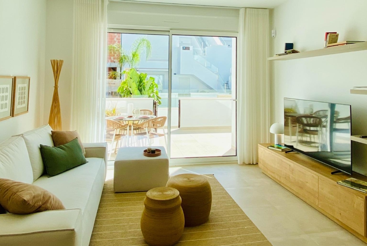 Sofa and TV unit facing sliding glass doors that open onto a sunny terrace dining area