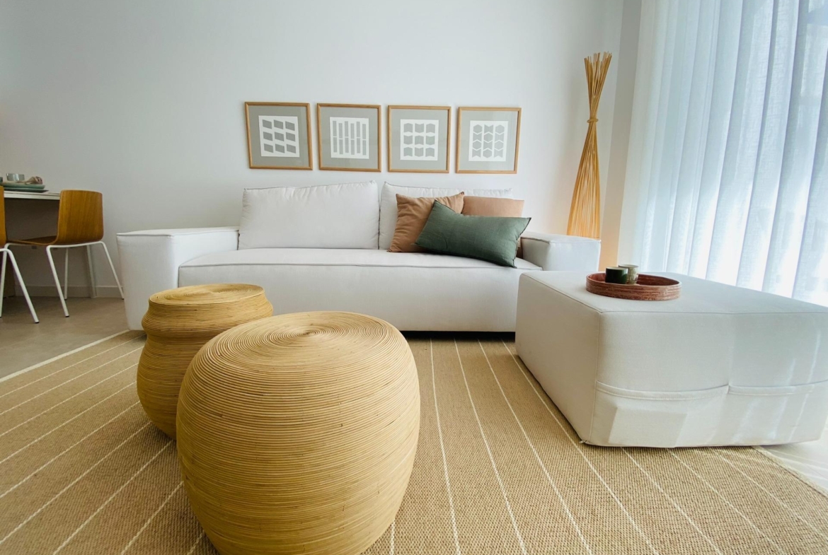 Neutral living room with white sofa, decorative round rattan stools and framed wall art