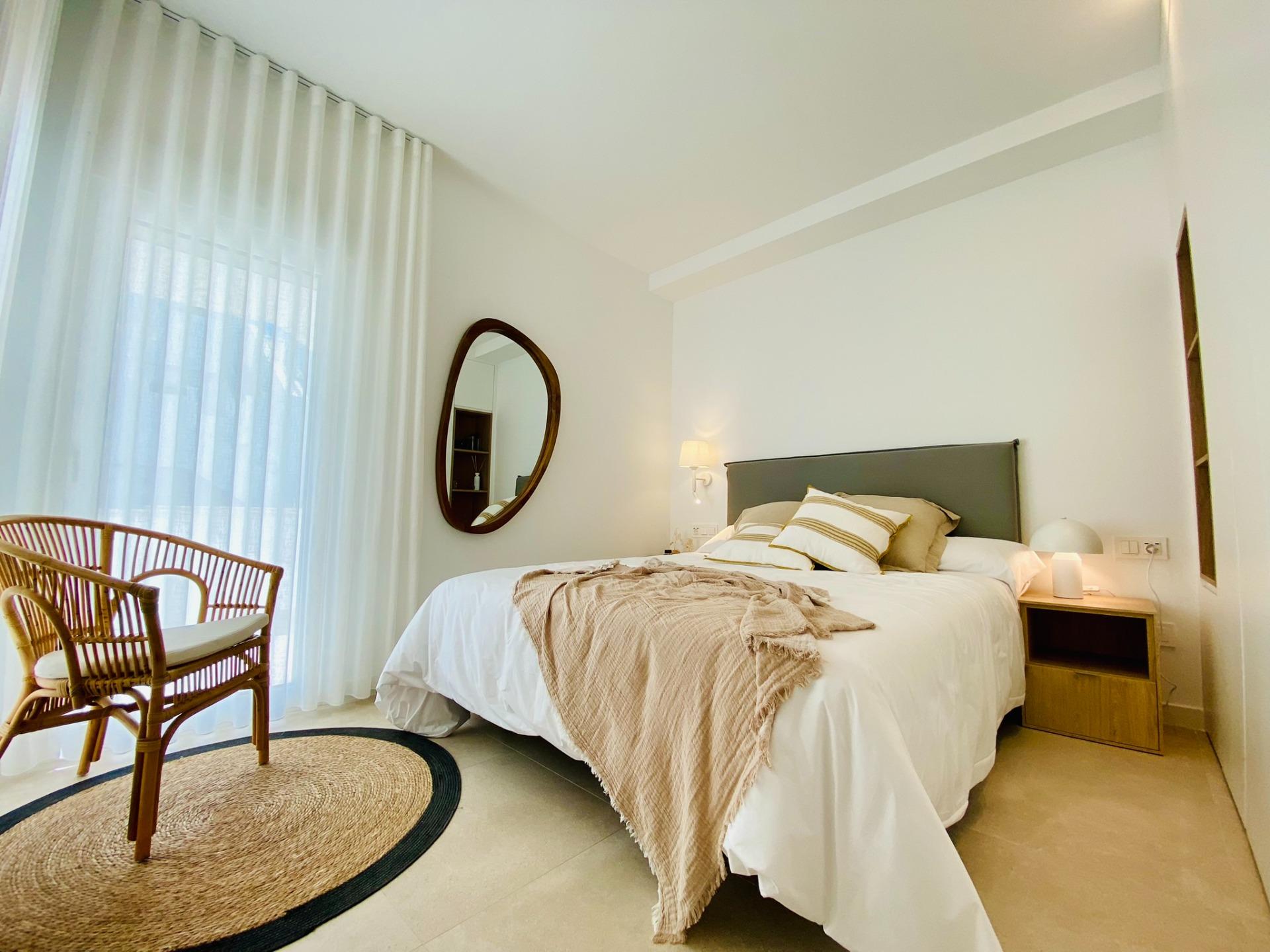 New-Build-Bungalows-in-Pilar-de-la-Horadada-Near-the-Beach-and-Town-Centre-11 Bright bedroom with double bed, bedside table, round wall mirror and wicker chair by window