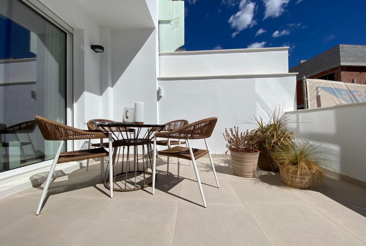 Private terrace with round outdoor dining table, woven chairs and potted plants against white walls