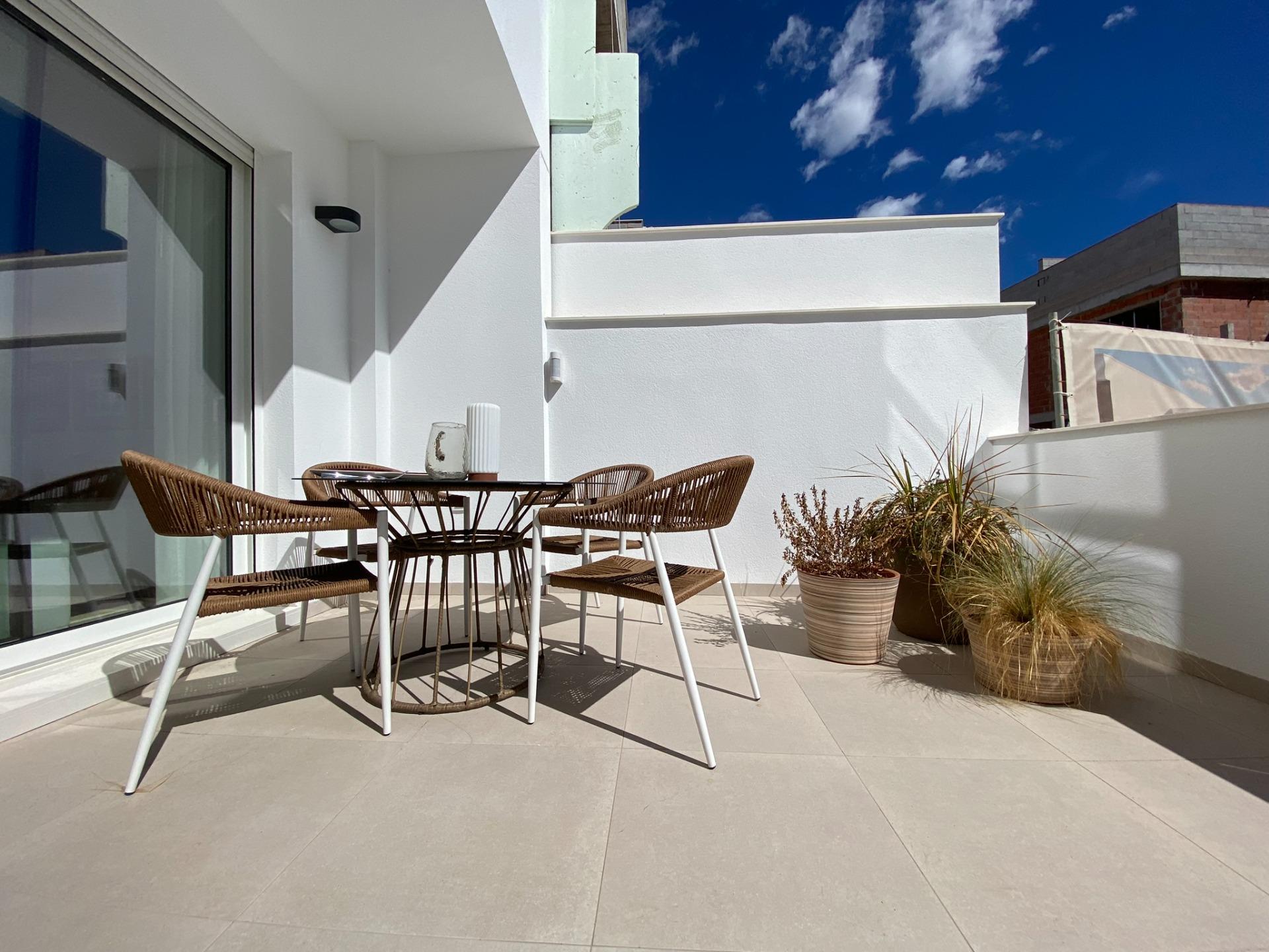 New-Build-Bungalows-in-Pilar-de-la-Horadada-Near-the-Beach-and-Town-Centre-13 Private terrace with round outdoor dining table, woven chairs and potted plants against white walls