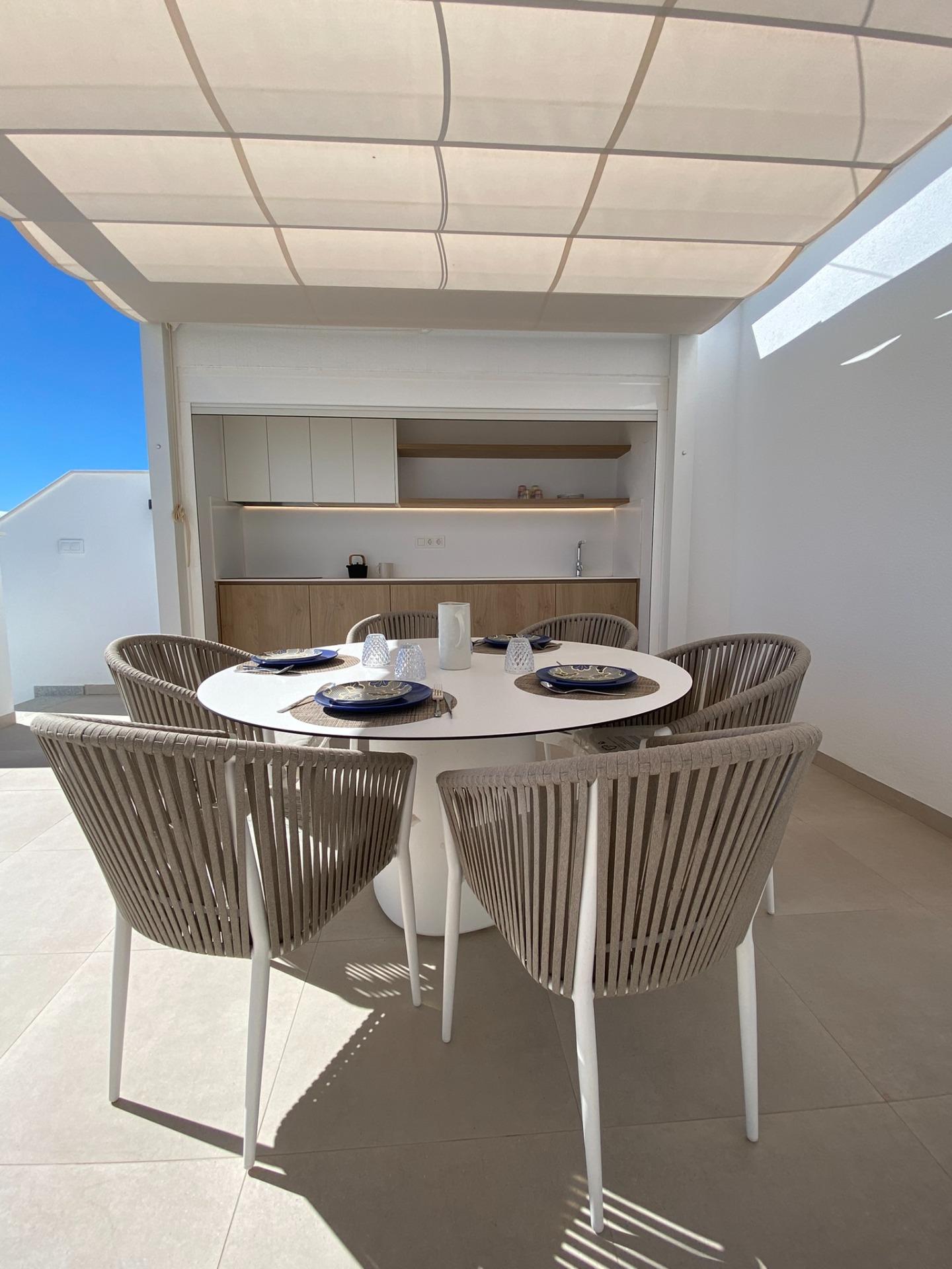 Round dining table and chairs beneath a fabric canopy with a kitchenette in the background