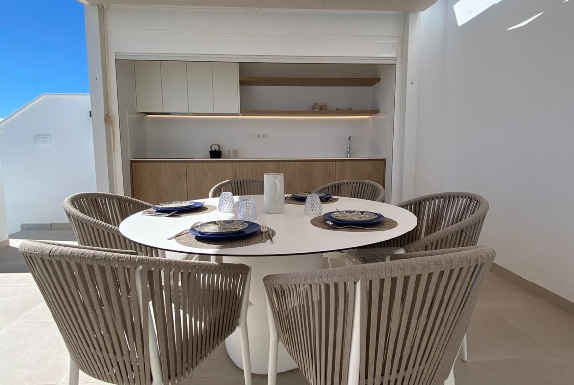 Shaded terrace dining area facing a small outdoor kitchenette under a fabric canopy.